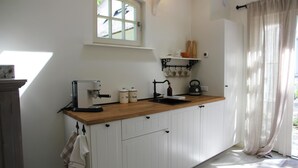 Een keuken met witte kastjes, een houten aanrecht, een koffieapparaat, een waterkoker en een raam met uitzicht op groen.
