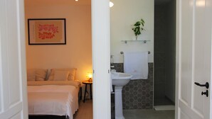 Een slaapkamer met een bed en nachtkastje, een badkamer met wastafel en toilet, en een gang met een deur.