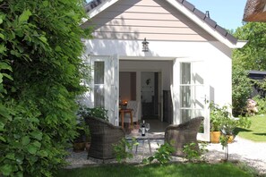 Uma casa com fachada branca, varanda com móveis de vime e um pequeno jardim.