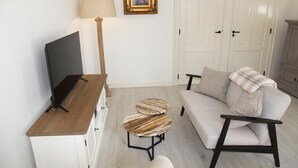 Een woonkamer met een televisie, een lamp, een bank en een klein rond tafeltje.