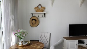 Een moderne woonkamer met een houten eettafel, grijze gestoffeerde stoelen, een televisie op een kast, en een decoratieve hoed aan de muur.