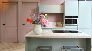 Een moderne keuken met een centraal eiland, twee barkrukken, een roestvrijstalen oven en een bloevas op het eiland.