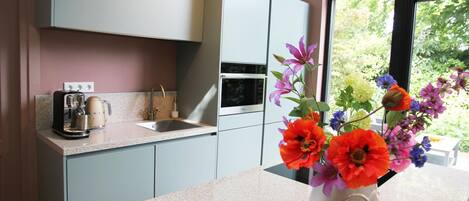 A kitchen with a countertop, a sink, a coffee maker, and a vase with flowers.
