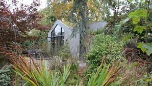 Een modern huis met een schuin dak en grote ramen, omringd door weelderige begroeiing en een tuin.