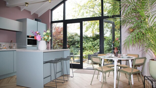 Een moderne keuken met een groot kookeiland, barkrukken en een eethoek met een ronde tafel en stoelen.