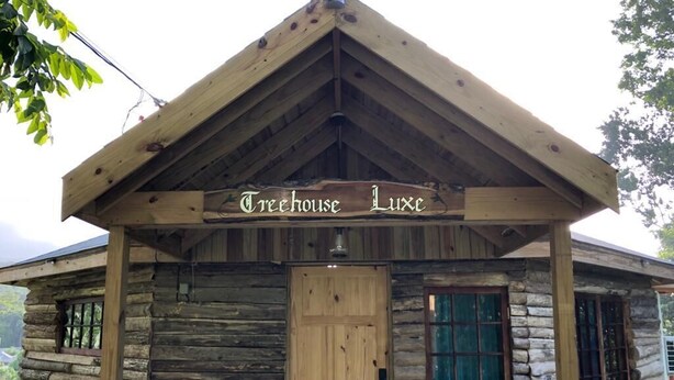 A rustic log cabin with a wooden door and a sign that reads "Creehouse Luxe".