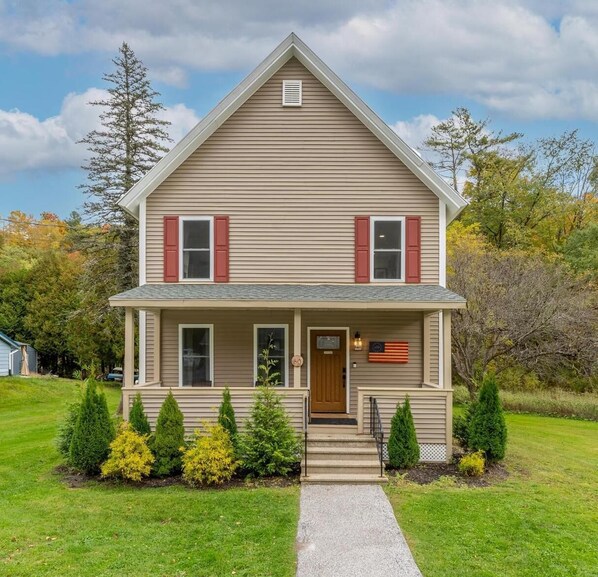 A two-story house with a front porch, a small front yard with shrubs, and a clear sky. - Feel the real VT! Lakes, hikes, a foodies delight! (Proctor)