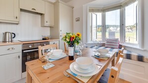 Una cocina moderna con armarios blancos, una mesa de comedor preparada para dos personas y vistas al exterior a través de grandes ventanales.