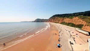 Una playa con una extensa franja de arena, un acantilado rocoso y un edificio con un área cubierta.