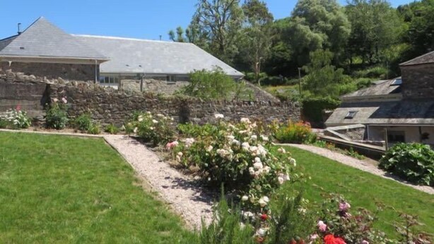 A stone house with a sloped roof, surrounded by a well-maintained garden with various plants and flowers.