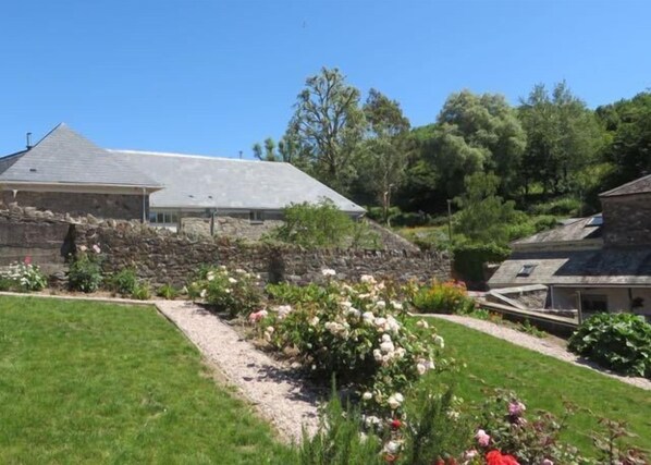 A stone house with a sloped roof, surrounded by a well-maintained garden with various plants and flowers.