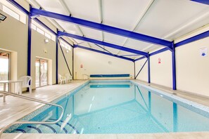 An indoor swimming pool with a clear blue water, surrounded by blue structural beams, and a tiled floor.