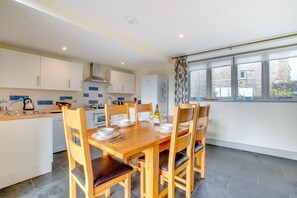 A modern kitchen with white cabinets, a wooden dining table set for four, and a window with a view of the outside.