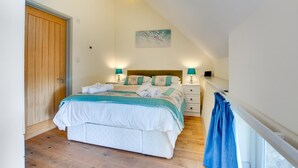 A bedroom with a bed, bedside tables, a lamp, a painting, and a wooden door.