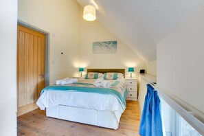 A bedroom with a bed, bedside tables, a lamp, a painting, and a wooden door.