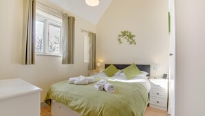 Een slaapkamer met een bed, nachtkastjes, een raam met gordijnen en een aan de muur bevestigde plant.