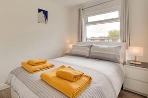 Une chambre d’hôtel avec un lit, deux lampes de chevet, une fenêtre avec des rideaux et un tableau au mur.