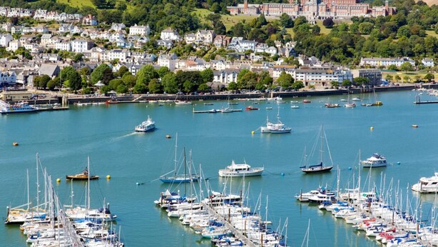Un port de plaisance où sont amarrés de nombreux bateaux, entouré d’une ville où se trouvent des bâtiments historiques et de nombreux espaces verts.