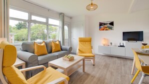 Un salon moderne avec un canapé gris, des fauteuils jaunes, une table basse en bois et un coin repas avec une chaise jaune.