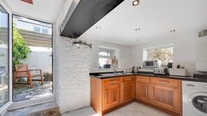 A modern kitchen with wooden cabinets, a built-in washing machine, and a large window. - 3 Bed in Brixham (oc-sdbell) (Brixham)