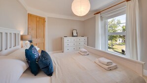 A bedroom with a bed, a dresser, a nightstand, a lamp, and a window with curtains. - 3 Bed in Brixham (oc-sdbell) (Brixham)