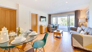 Un salon moderne avec une table à manger en verre, des chaises de couleur turquoise, un canapé et un téléviseur fixé au mur.