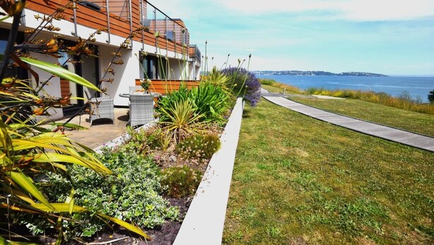 Une maison moderne dotée d’un balcon donnant sur un espace verdoyant et un plan d’eau.