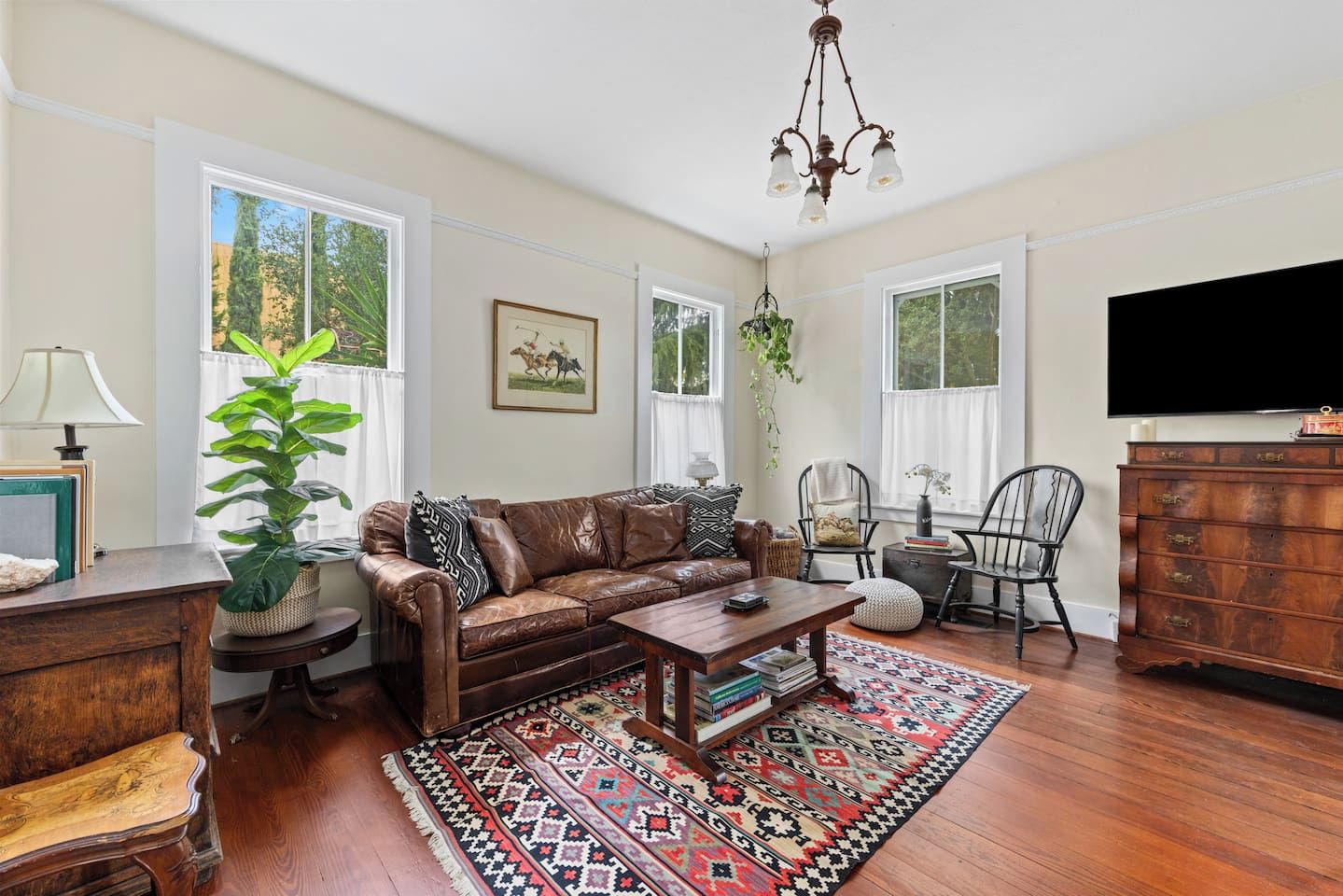 A living room with a brown leather sofa, a wooden coffee table, a patterned rug, and a television on the wall.