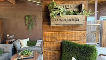Parede de madeira rústica com uma placa antiga que diz '1876 LOS ALAMOS' e um vaso com plantas verdes.