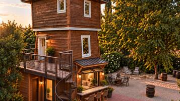 A two-story wooden house with a balcony, outdoor seating area, and a spiral staircase.