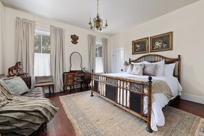 Un dormitorio con una cama grande, un aparador de madera, un tocador con espejo y un chaise lounge.