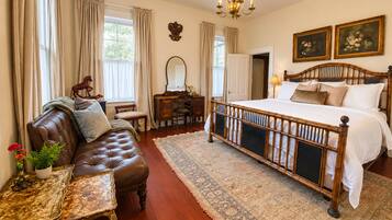A bedroom with a large bed, a leather sofa, a desk, and a chandelier.