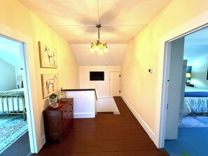 A hallway with a wooden floor, a white door, a white wall with a mounted picture, and a ceiling light fixture. - Heritage House ~ Living Art ~ Steps from Bell St (Los Alamos)