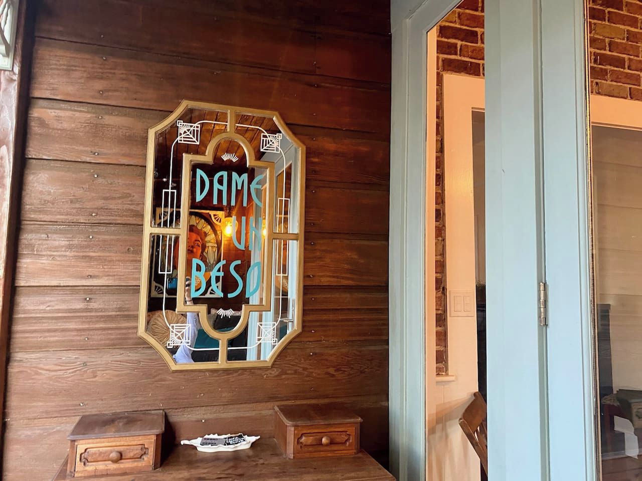 Pared de madera con un letrero enmarcado que dice 'DAME UN BESO'.