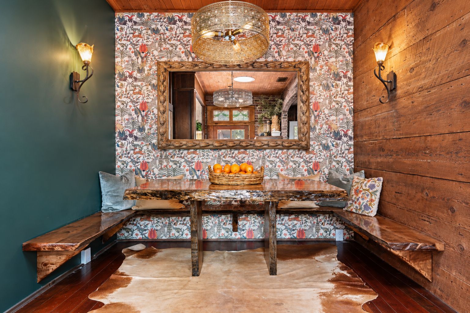 Un intérieur rustique avec un banc en bois, une table à manger sur laquelle est posé un panier de fruits, et un miroir décoratif au-dessus de la table.