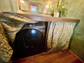 Une pièce de taille modeste, équipée d’un lave-linge, d’un comptoir en bois et de rideaux à motifs.