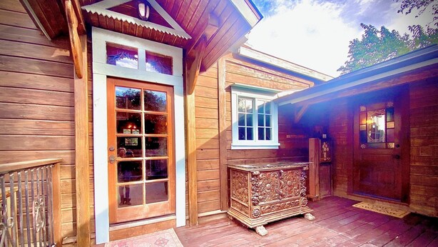 A wooden cabin with a large glass door, a small window, and a decorative cabinet on the porch. - 1882 Heritage House ~ Porches, Gardens & Bali Bed (Los Alamos)