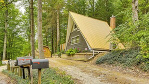 Een chalet met een schuin dak, omringd door bomen, en een grindpad ernaartoe.