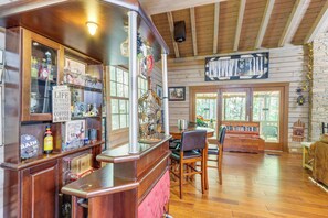 A rustic interior with wooden floors, a bar area with wine and coffee, and a large window with a view of trees. - Ellijay Getaway: Fire Pit + Hot Tub (Ellijay)
