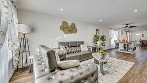 Ein modernes Wohnzimmer mit einem grauen Ecksofa, einem runden Couchtisch und einem Essbereich mit Tisch und Stühlen.