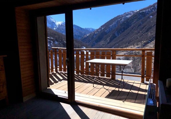 Une terrasse en bois avec une table et des chaises, offrant une vue sur un paysage montagneux.