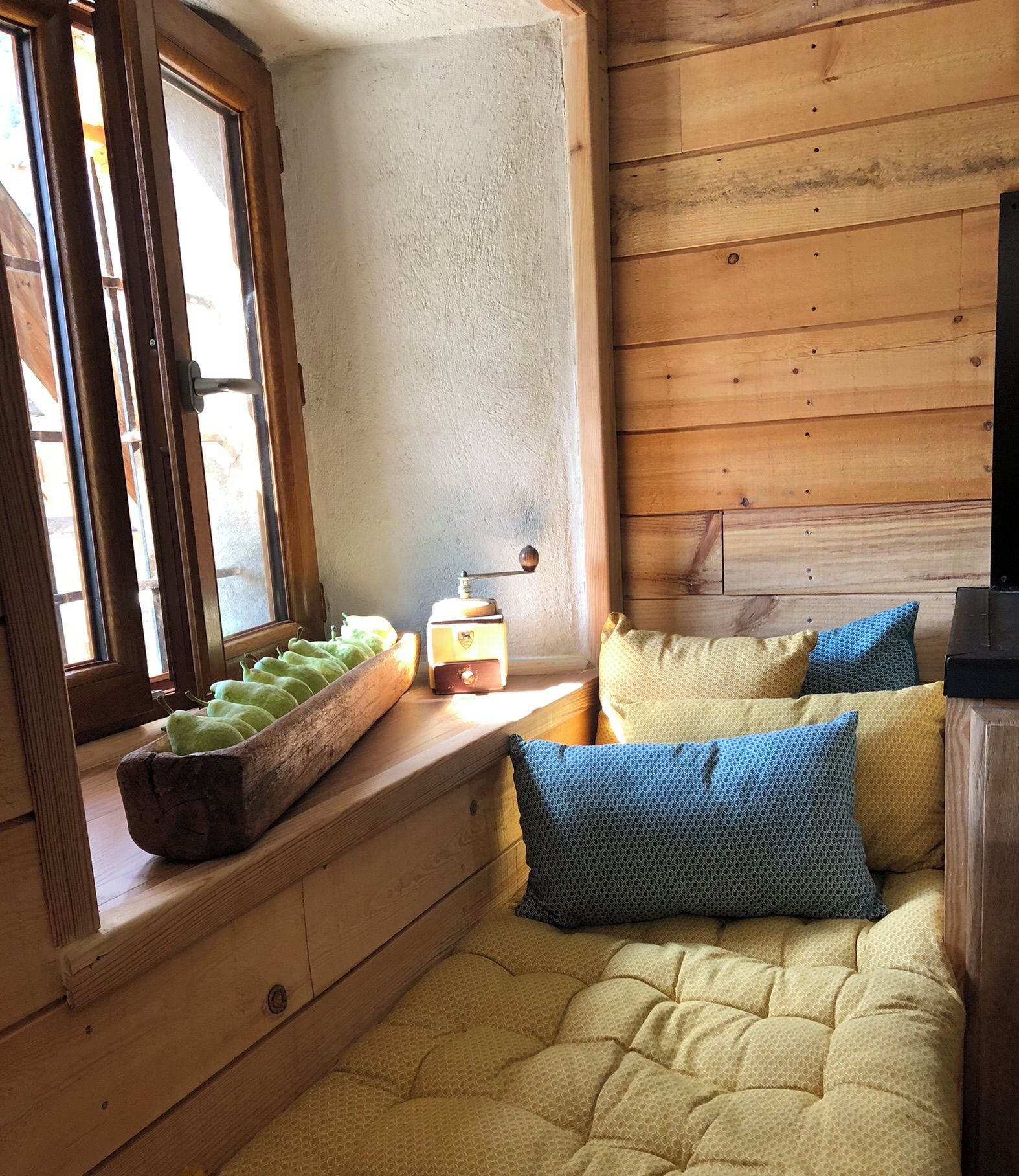 A cozy reading nook with a wooden bench, a small table with a book, and a window with a view of the mountains.