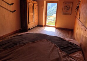 Une chambre avec une armoire en bois, un lit et une fenêtre donnant sur un paysage montagneux.