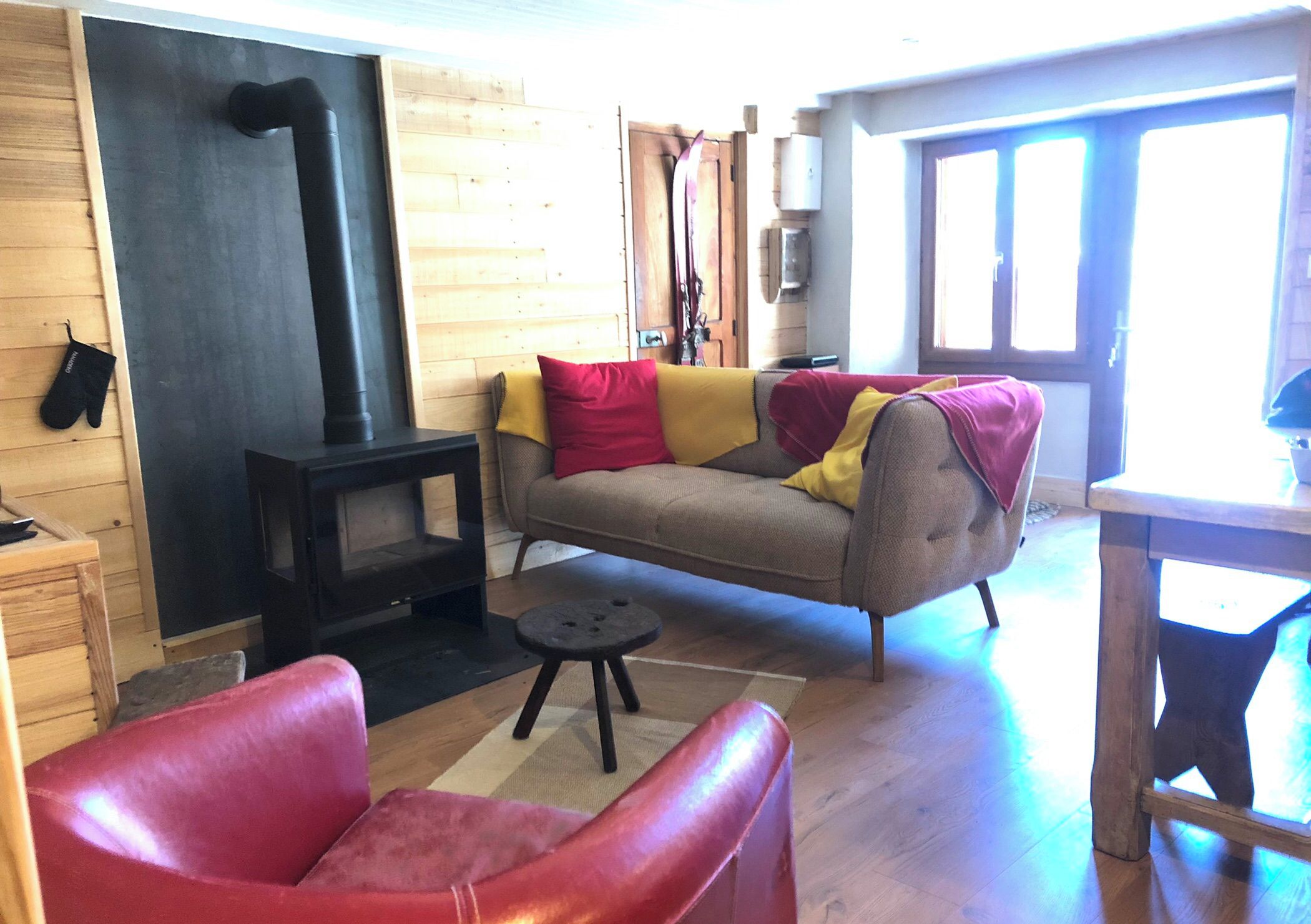 Un salon chaleureux avec un canapé, un fauteuil rouge, une cheminée et un mur en bois.