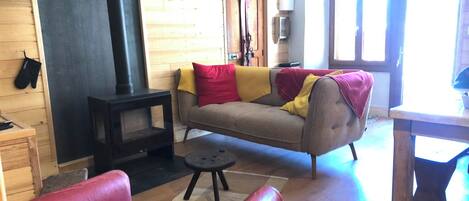 Un salon chaleureux avec un canapé, un fauteuil rouge, une cheminée et un mur en bois.