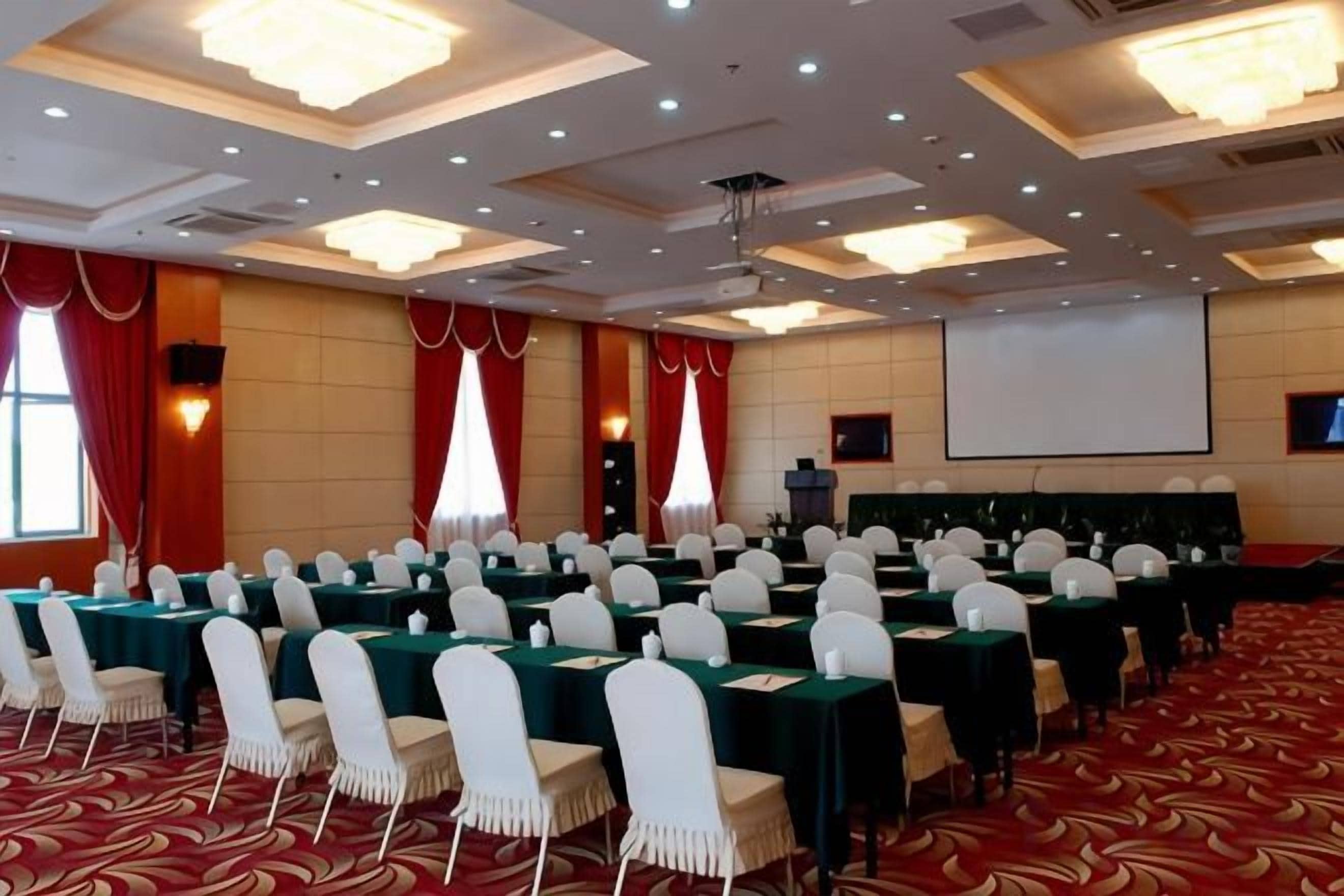 A conference room with rows of tables and chairs, a projector screen, and a large screen.