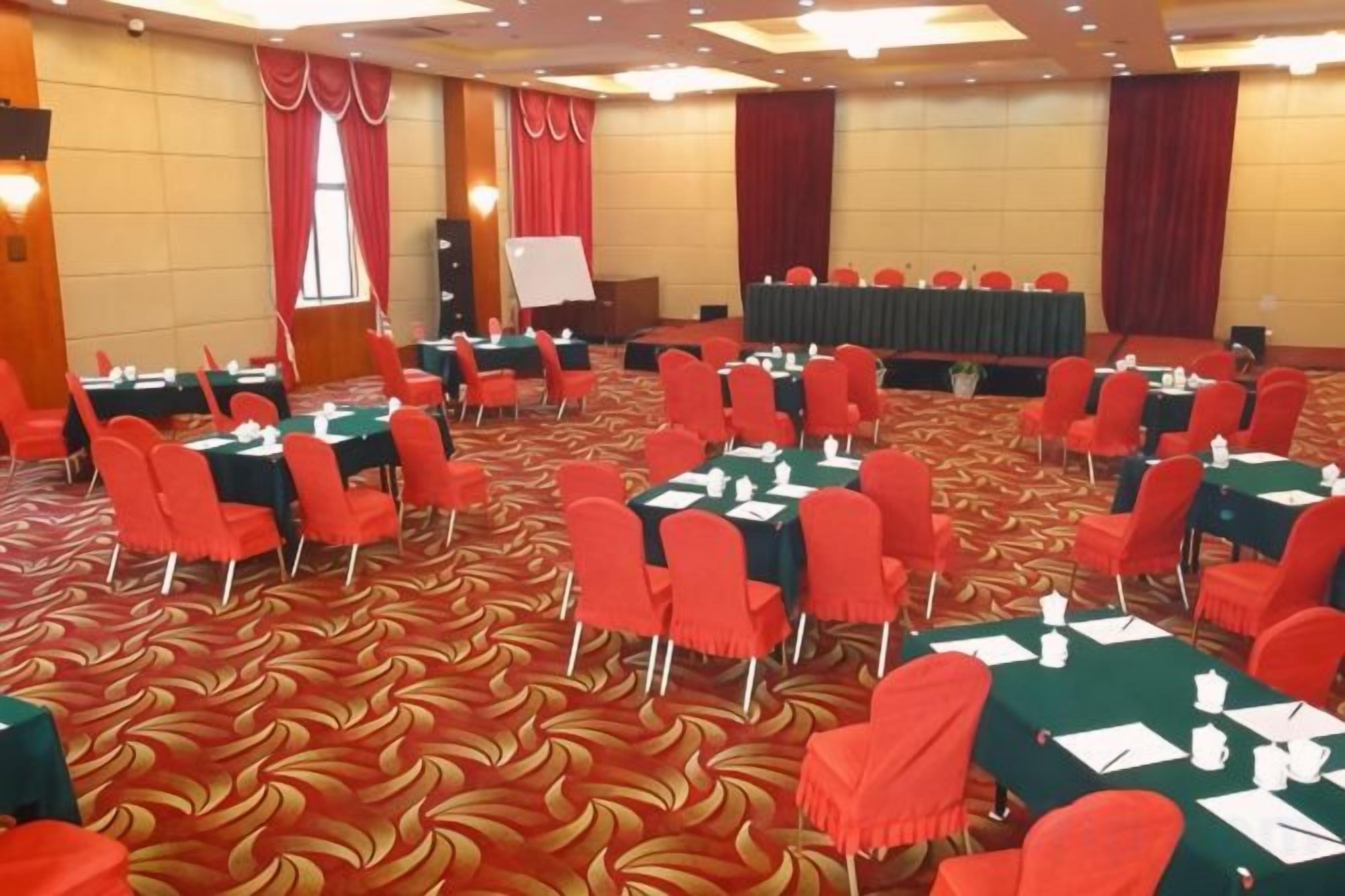 A conference room with round tables and red chairs, carpeted floor, and a stage with a whiteboard.