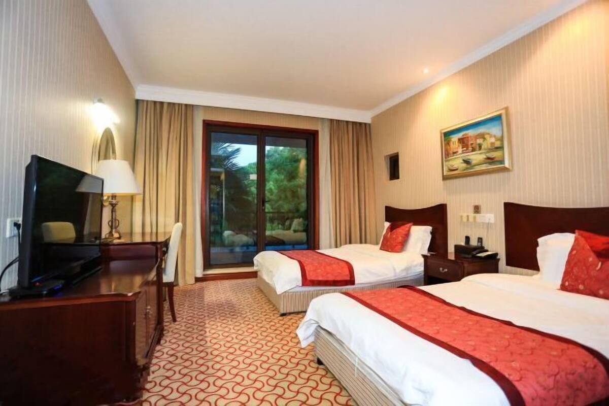 Habitación de hotel con dos camas, un escritorio, un televisor, una lámpara y un cuadro en la pared.
