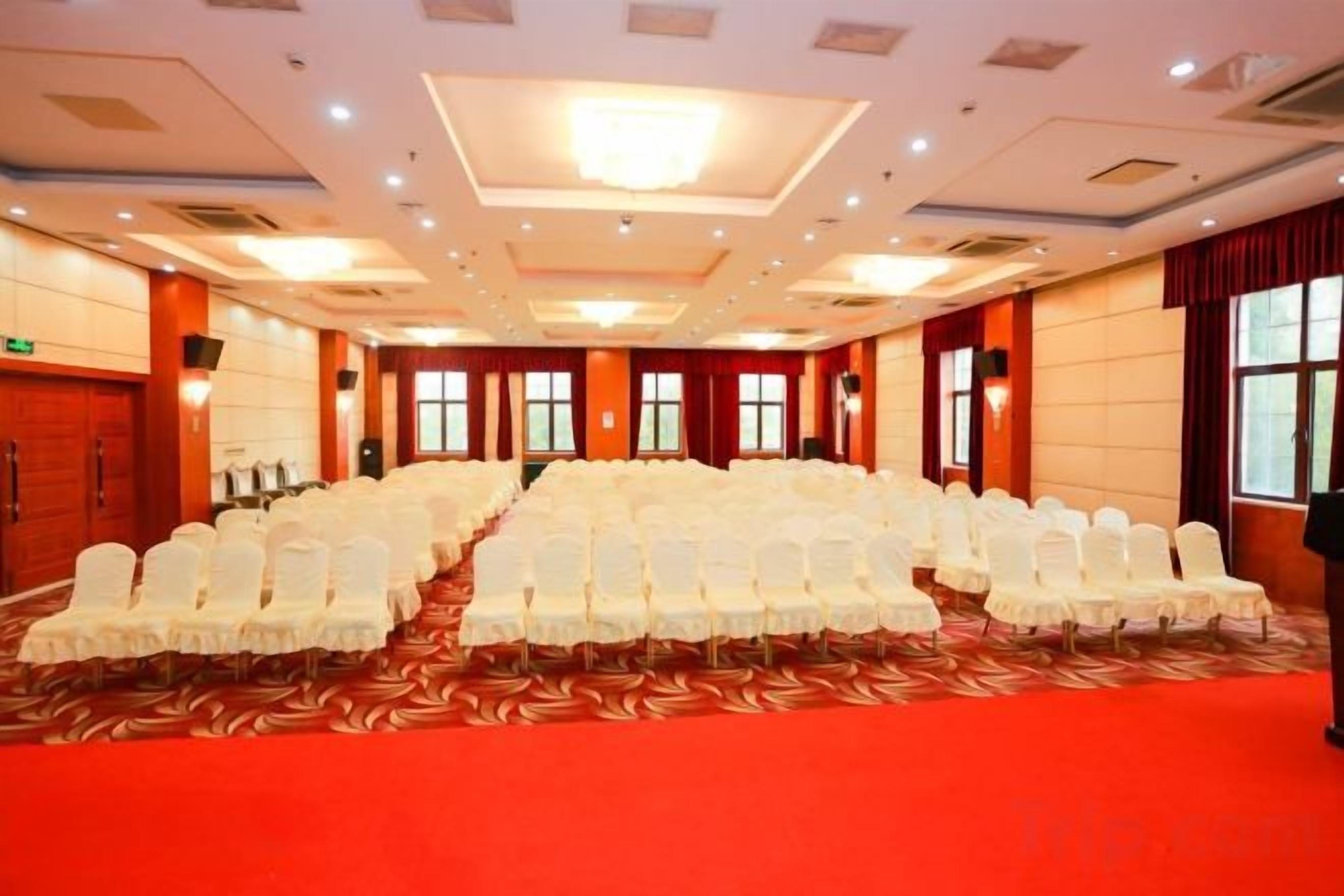 A conference room with rows of white chairs, a red carpet, and a high ceiling with recessed lighting.