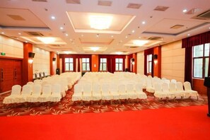 Une salle de conférence avec des rangées de chaises blanches, une moquette rouge et un plafond haut doté d’un éclairage encastré.